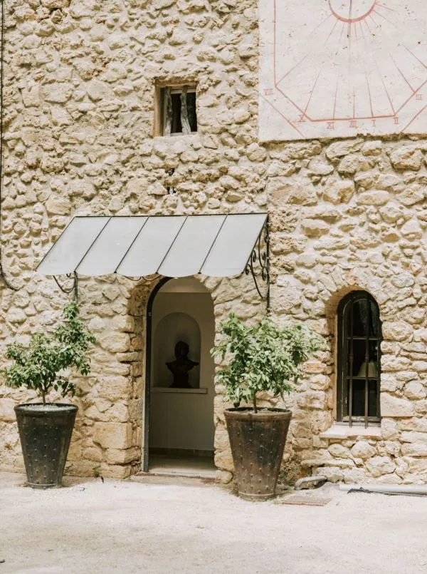 La façade en pierre de la bastide, son cadran solaire et ses oliviers en pot