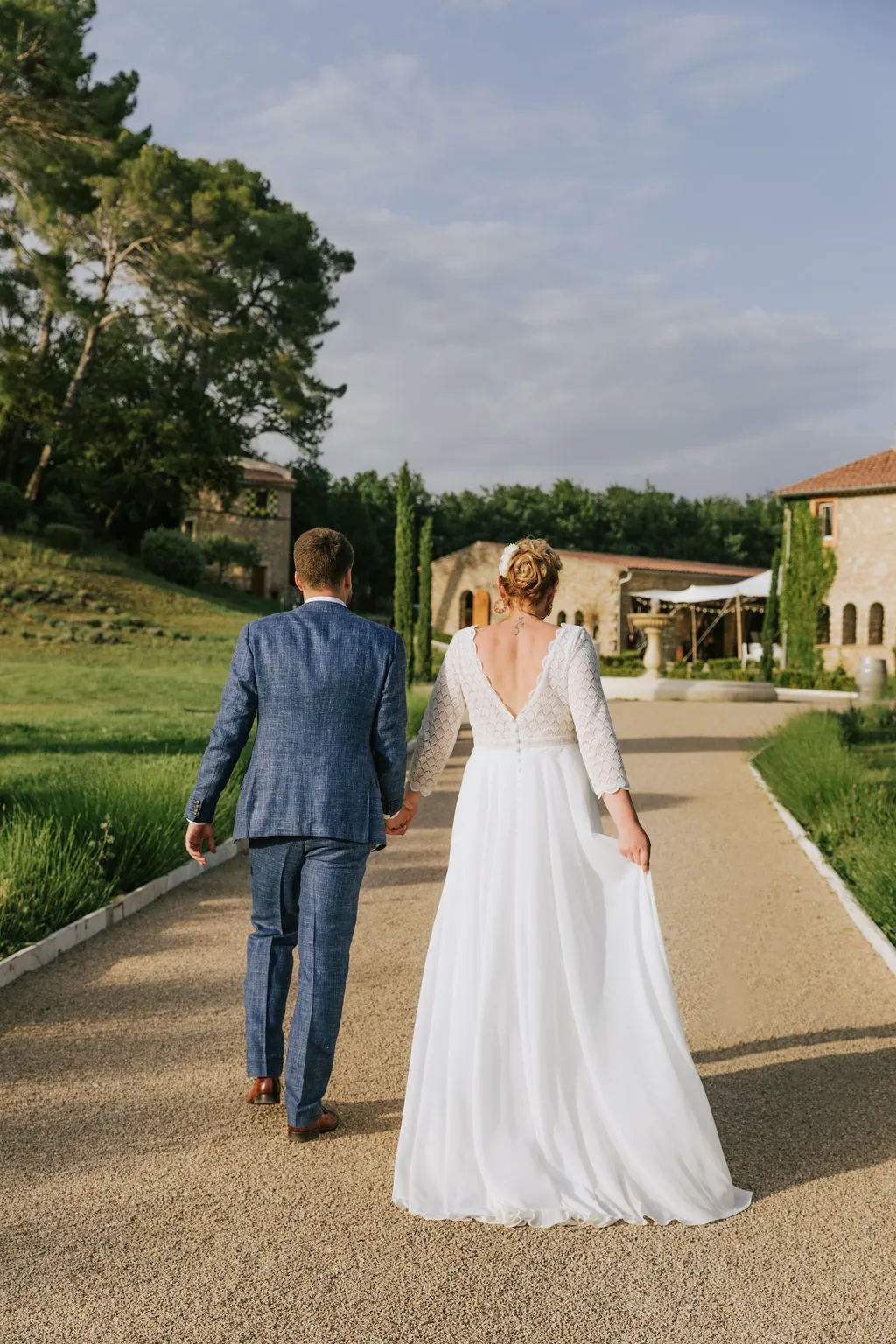 Un couple de mariés marche main dans la main vers la bastide